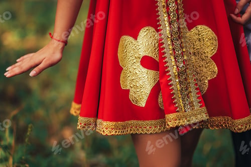 Preview: Girl in national Russian clothes of red color and golden ornaments on a background of green grass