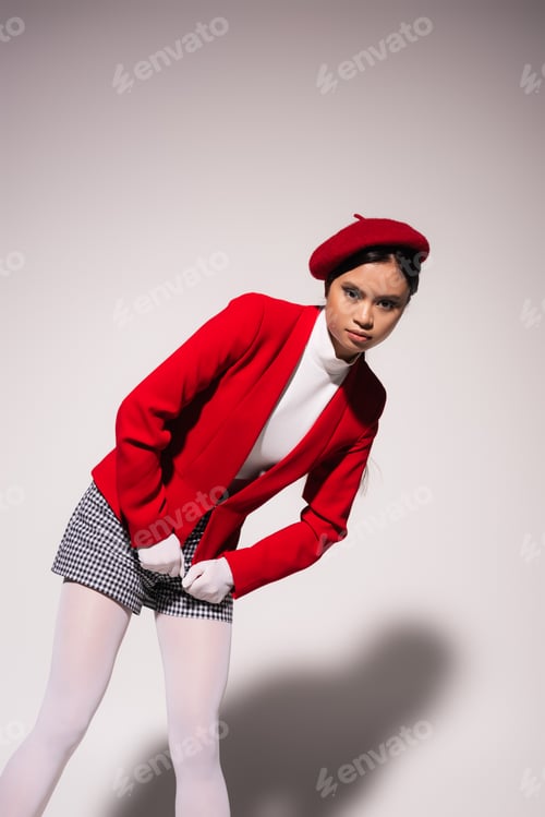 Preview: Pretty asian model in red jacket and plaid shorts posing on grey background