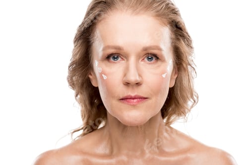 Preview: mature woman with cosmetic cream on face looking at camera Isolated On White