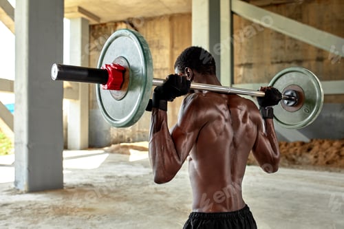 Preview: Athletic black young man lifting a heavy-weight barbell in outdoor gym under the bridge. Healthy