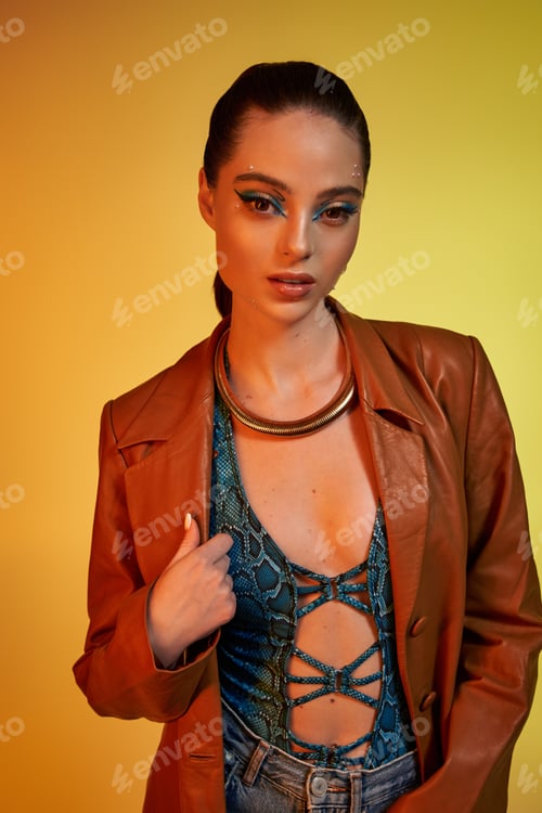 Preview: A young woman poses confidently in fashionable snake print attire against a bright yellow backdrop.