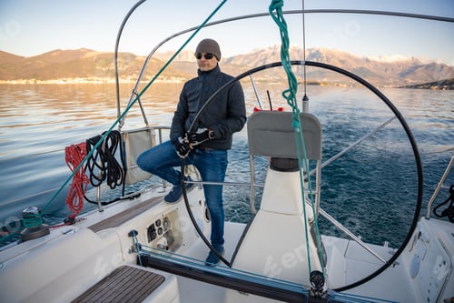 Preview: Young man captain standing at the helm and controls a sailboat during a journey by sea in winter
