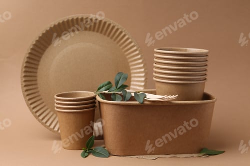 Preview: Set of disposable tableware and green leaves on brown background