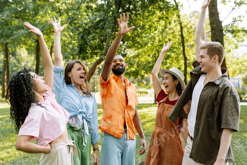 Preview: Group of five young adults raising hands and cheering in a park