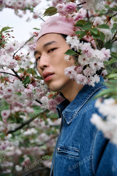 Preview: Young Asian man showcases stylish denim in a vibrant flower-filled park setting