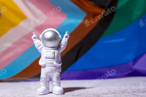 Preview: Toy astronaut on Rainbow LGBTQIA flag made from silk material background. Happy pride month. Symbol