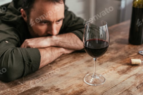 Preview: Selective focus of pensive man looking at wine glass on table