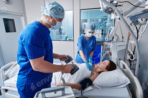Preview: Doctor holding defibrillator on unconscious female patient's chest in intensive care unit during
