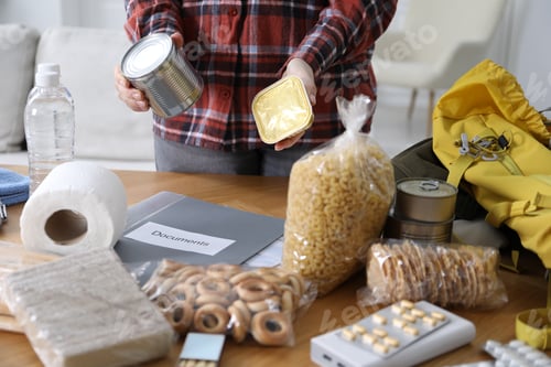 Preview: Survival kit. Woman packing different emergency supplies at wooden table indoors, closeup