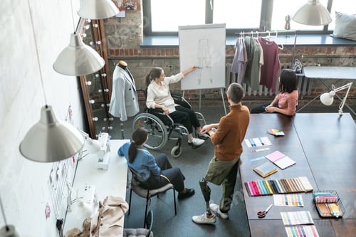 Preview: Young creative designer in wheelchair pointing at sketch on whiteboard while making presentation