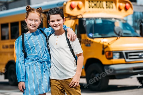 Preview: happy little scholars embracing and looking at camera in front of school bus