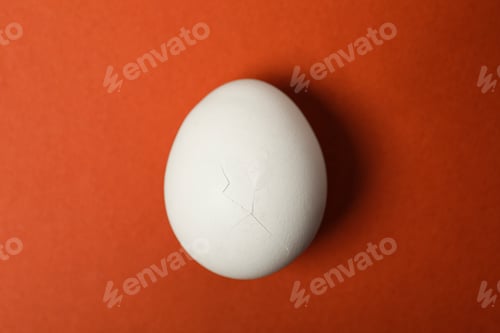 Preview: One egg with cracked shell on red background, top view