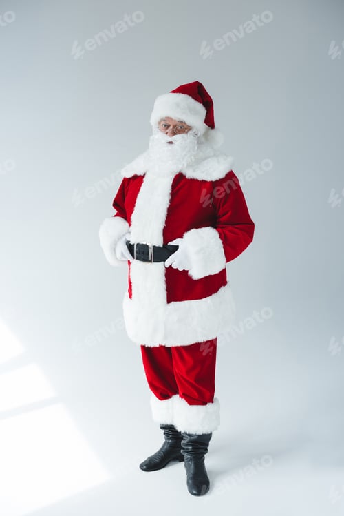Preview: confident bearded santa claus adjusting belt and looking at camera isolated on white