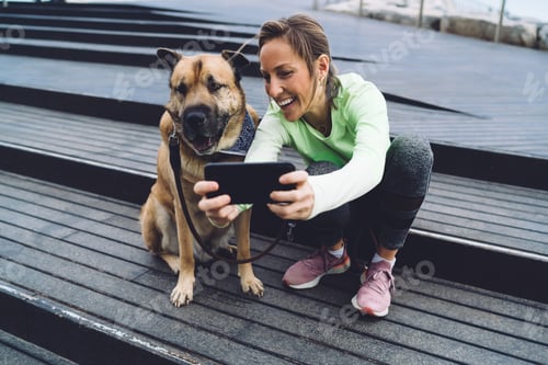 Preview: Happy woman with dog using smartphone on street