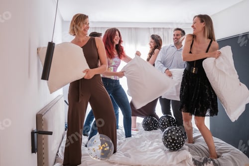 Preview: Group of young friends at a party jumping on the bed and fighting with pillows. Concept: happy