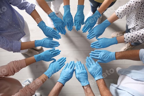 Preview: People in blue medical gloves joining hands indoors, top view