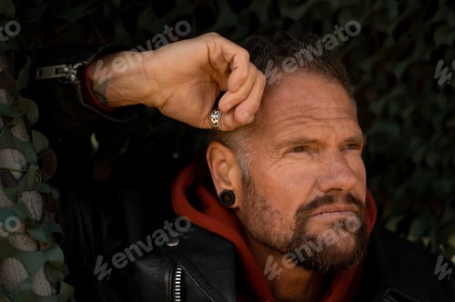 Preview: Portrait of a handsome man wearing a black leather jacket, a trimmed beard and black earrings.