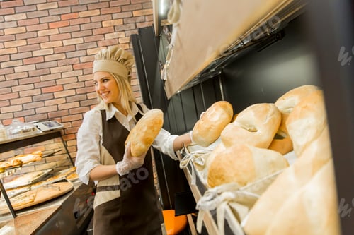 Preview: Young woman takes fresh bread from the shelves in a baker shop