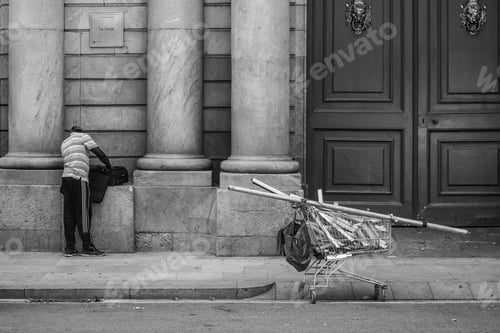 Preview: Man with an open suitcase on the columns of a building next to the cart filled with wooden pieces