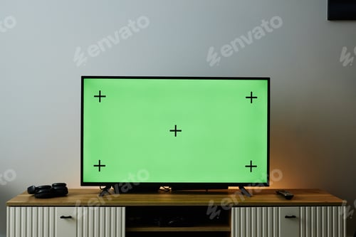 Preview: Big Flat Screen TV with Green Screen on Wooden TV Stand Against White Wall