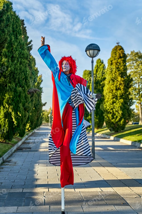 Preview: Creative clowns on stilts walking on pathway in sunny park