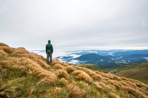 Preview: Male climber tourist standing on grassy hill slope on green mountains