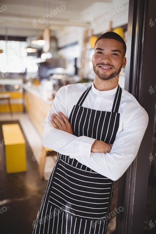 Preview: Portrait of handsome young waiter standing with arms crossed