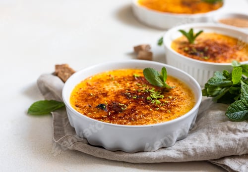 Preview: Creme brulee with caramel crust and mint in white ceramic dishes.