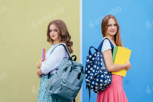 Preview: Two teenage girls with backpacks standing against colorful wall