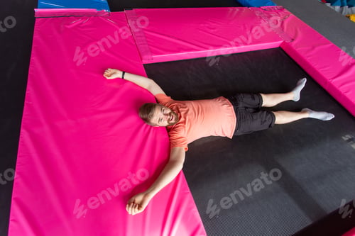 Preview: Fitness, fun, leisure and sport activity concept - Man lying on a trampoline indoors, top view