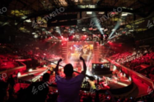 Preview: Abstract blurred background of big esports gaming event at big arena. Man with a hands raised