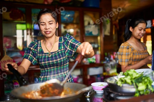 Preview: thai mother and daughter cooking together in rustic kitchen making red curry