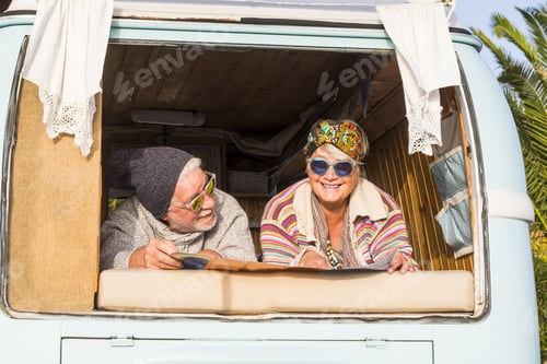 Preview: Happy senior retired couple in retro vintage style van or camper planning a trip looking at map