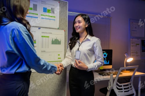 Preview: Two businesswomen shaking hands after successful agreement about new project in office at night