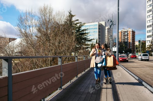 Preview: Two mature women walking, talking and using smartphone after shopping