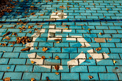 Preview: High angle shot of the wheelchair symbol painted on the ground under the sunlight in autumn