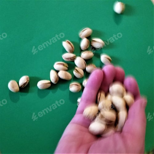 Preview: Hand Holding Pistachios on a Green Background