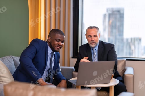Preview: Two businessmen sitting on sofa working discuss on financial forecast together on laptop information