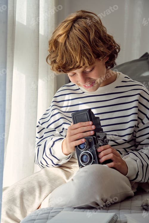 Preview: Smiling boy with aged photo camera on bed