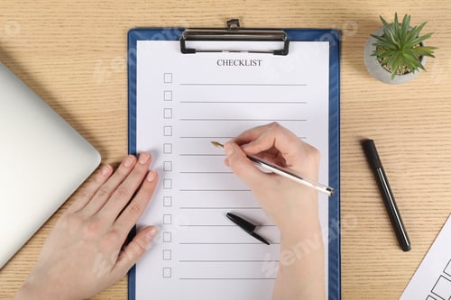 Preview: Woman filling Checklist with pen at wooden table, top view
