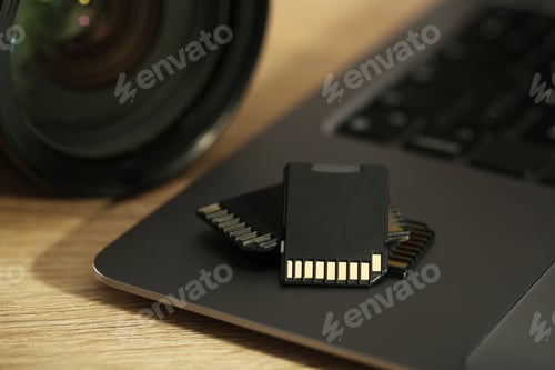 Preview: SD memory cards, laptop and photo camera on wooden table, closeup