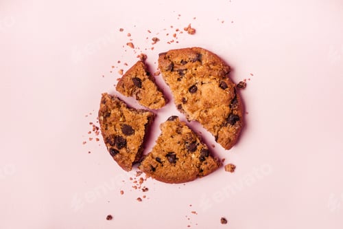 Preview: Broken chocolate chip cookie and crumbs on pink background