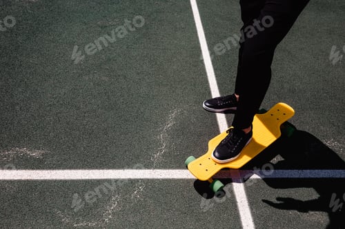 Preview: Close up photo of modern man in stylish wear keeping feet on yellow skateboard