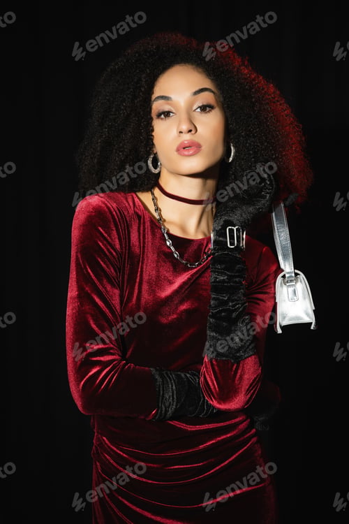 Preview: Fashionable african american model in burgundy dress and handbag isolated on black