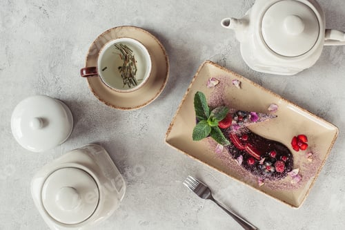 Preview: food composition with piece of blueberry cake served with mint leaves and violet petals on plate,