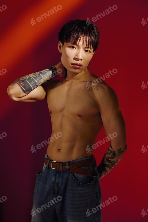 Preview: Stylish young Asian man posing confidently against a stunning red backdrop in evening light
