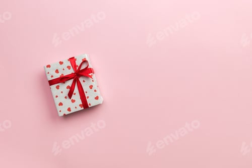 Preview: Gift box with red ribbon and heart on pink background, top view with copy space for text