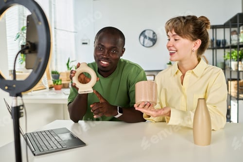 Preview: Happy young intercultural couple with handmade vases talking to online audience