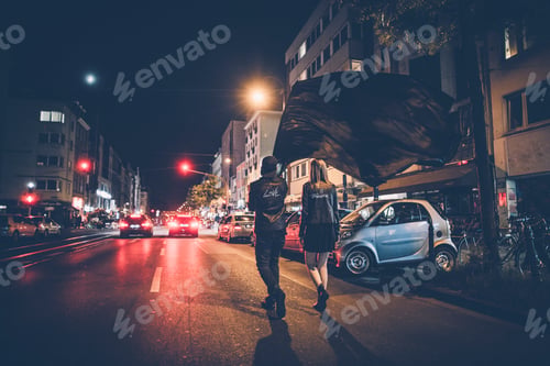 Preview: Back view of young couple with black flag walking on the street by night