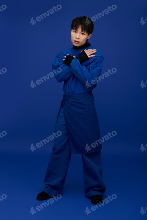 Preview: Young handsome Asian man poses confidently in stylish blue outfit against solid backdrop